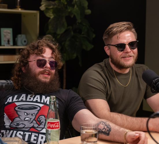 Two members of the Alabama Twisters sit at a podcast table during an interview, wearing sunglasses and speaking into microphones.