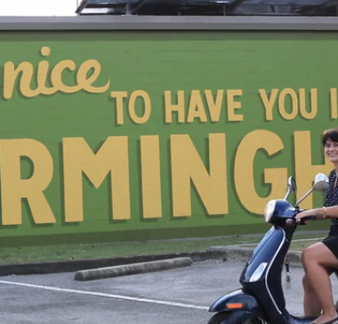 carrie rollwagen driving a vespa in front of birmingham mural