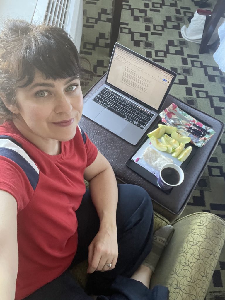 girl in a hotel room with a laptop and a snack